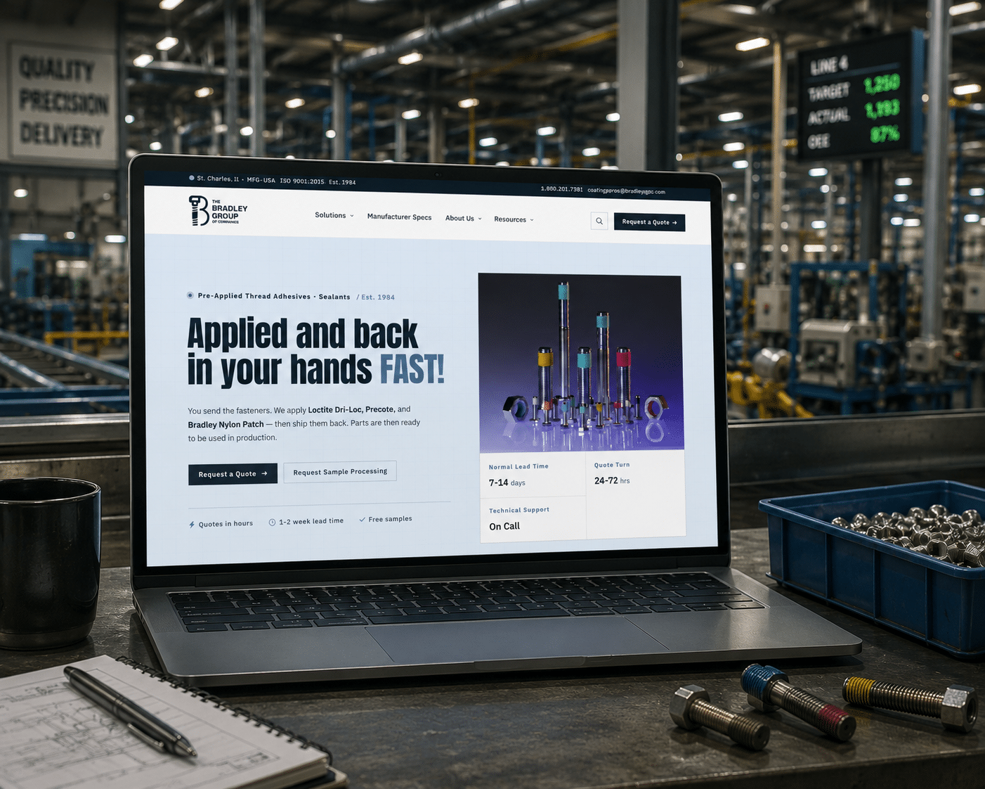 A laptop on a workshop table displays an industrial website for threaded fasteners. The background shows a factory with machines, trays of metal parts, and a digital wall sign showing production stats.